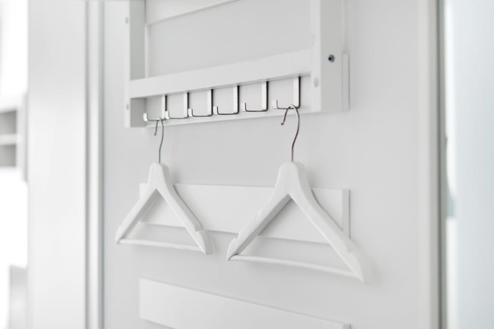 two white wooden hangers hanging on a hook on a white wall in hallway, no people, closeup