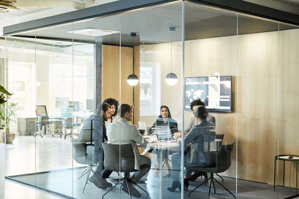 business colleagues sitting at conference table seen through glass wall multi ethnic coworkers are discussing in board room at office they are planning strategy