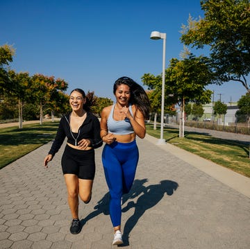 Cheerful female friends running on footpath at park amigas corriendo pasandolo bien