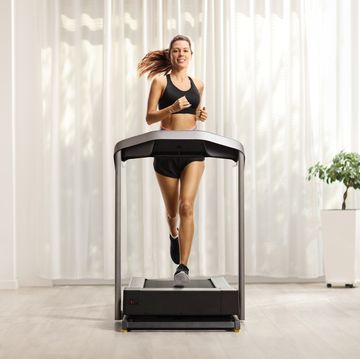 full length portrait of a young woman in shorts and top running on a treadmill at home