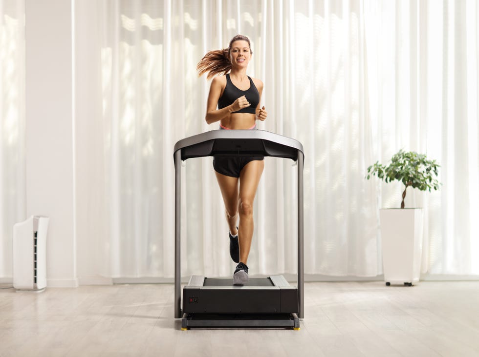 full length portrait of a young woman in shorts and top running on a treadmill at home