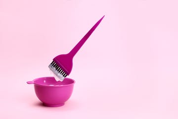 brush levitating over a plastic bowl of hair dye on a pink background