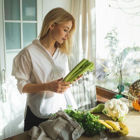 smiling young blonde woman organising fruits and vegetables from a reusable shopping bag on the kitchen table after grocery shopping zero waste concept vegan, vegetarian people nutritionist occupation