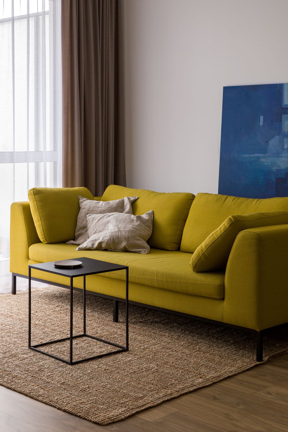 bright living room with modern yellow sofa, simple, cubic, black coffee table and natural rug