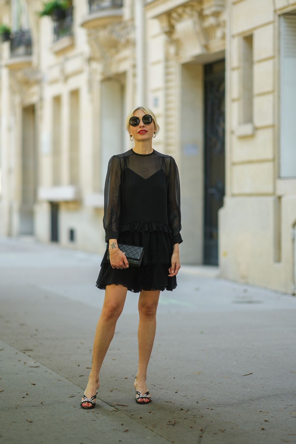 paris, france   june 10 emy venturini wears black sunglasses from linda farrow  the row, gold earrings, a saint laurent ysl necklace, a black silk tank top, a black transparent top dress with ruffle short skirt from miu miu, a gold ring, a gold chain bracelet, a black shiny grained leather chanel clutch bag, black shiny leather strappy pumps shoes with rhinestones on the straps from miu miu, on june 10, 2021 in paris, france photo by edward berthelotgetty images