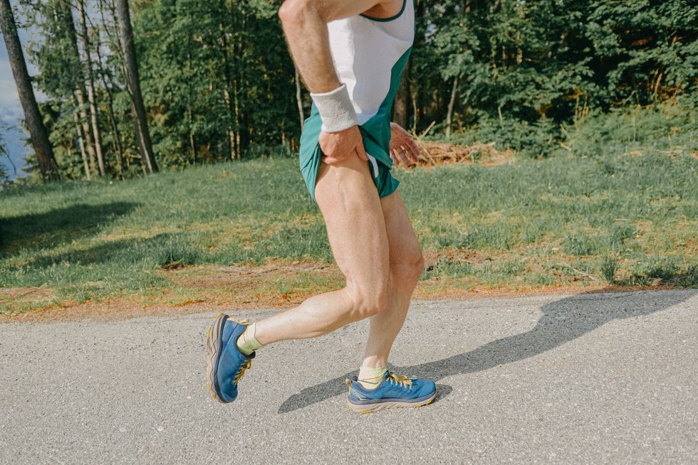 lower section of a middle age man running on the side of a mountain road he is touching his right hip, on which is visible a scar from a previous surgery