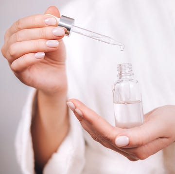 Woman in white bathrobe with nude pink manicure holds pipette and transparent glass bottle with natural essential oil or organic serum. She ready to start skin care procedures. Concept of home body care and healthy lifestyle. Close-up front view woman in white bathrobe with nude pink manicure holds pipette and transparent glass bottle with natural essential oil or organic serum she ready to start skin care procedures concept of home body care and healthy lifestyle close up front view