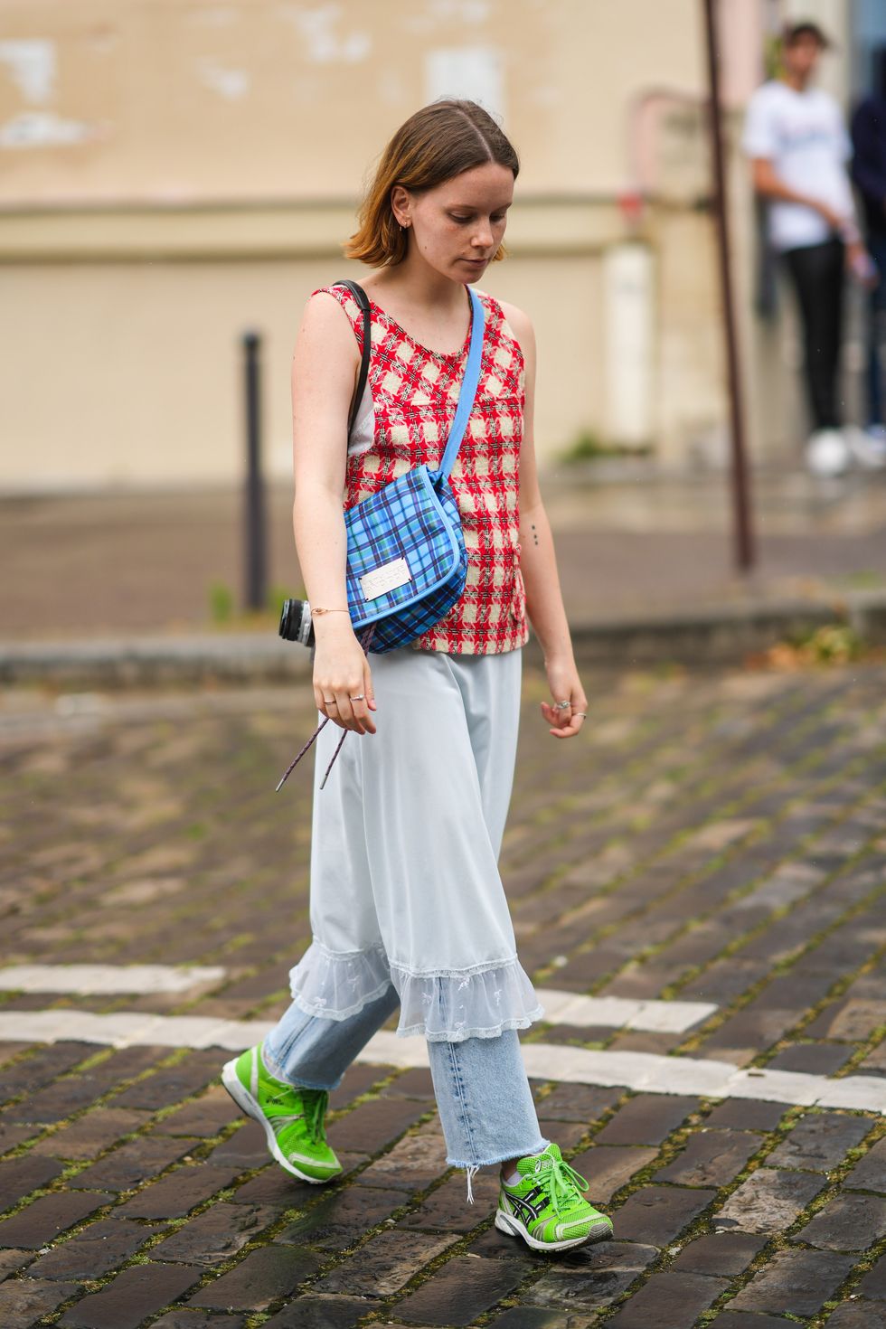 paris, france   june 26 a guest wears a beige and red wool print pattern tank top, a gold bracelet, a blue and burgundy checkered crossbody bag from neith nyer and ddp, a white lace tulle knees skirt, blue faded denim ripped mom jeans pants, silver rings, neon green fabric asics sneakers, outside hermes, during paris fashion week   menswear springsummer 2022, on june 26, 2021 in paris, france photo by edward berthelotgetty images