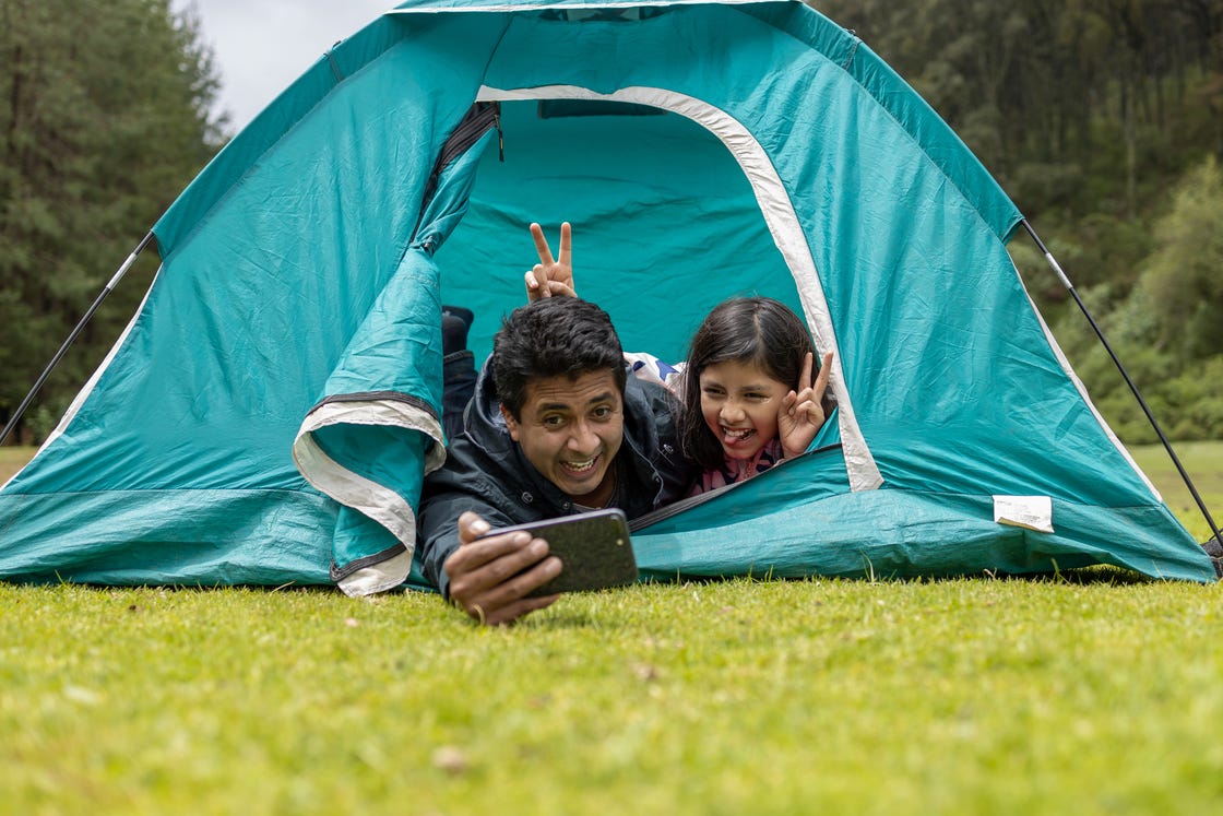 father and daughter taking selfie in camping tent