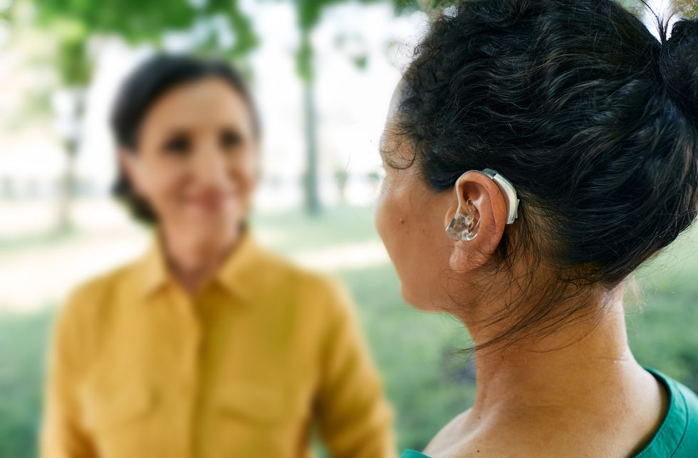 adult woman with a hearing impairment uses a hearing aid to communicate with her female friend at city park hearing solutions