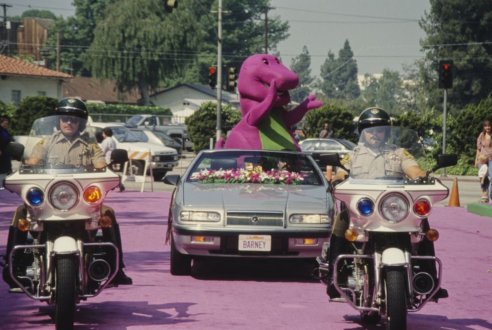 barney, the purple tyrannosaurus rex from childrens television series barney friends, riding in a convertible car following behind police outriders, at an unspecified event, location unspecified, circa 1995 photo by vinnie zuffantemichael ochs archivesgetty images