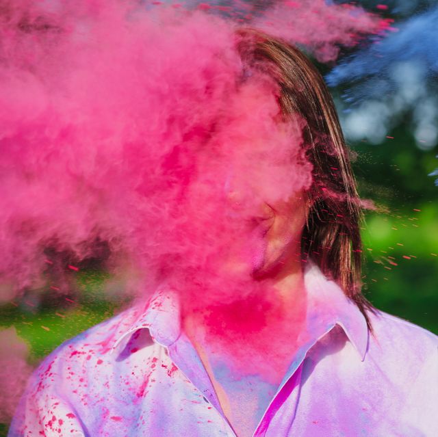 portrait of merry caucasian woman posing in a cloud of a pink  and blue dry paint at holi festival