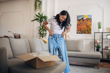 one woman, beautiful asian woman standing in living room at home she is trying on denim pants that she ordered