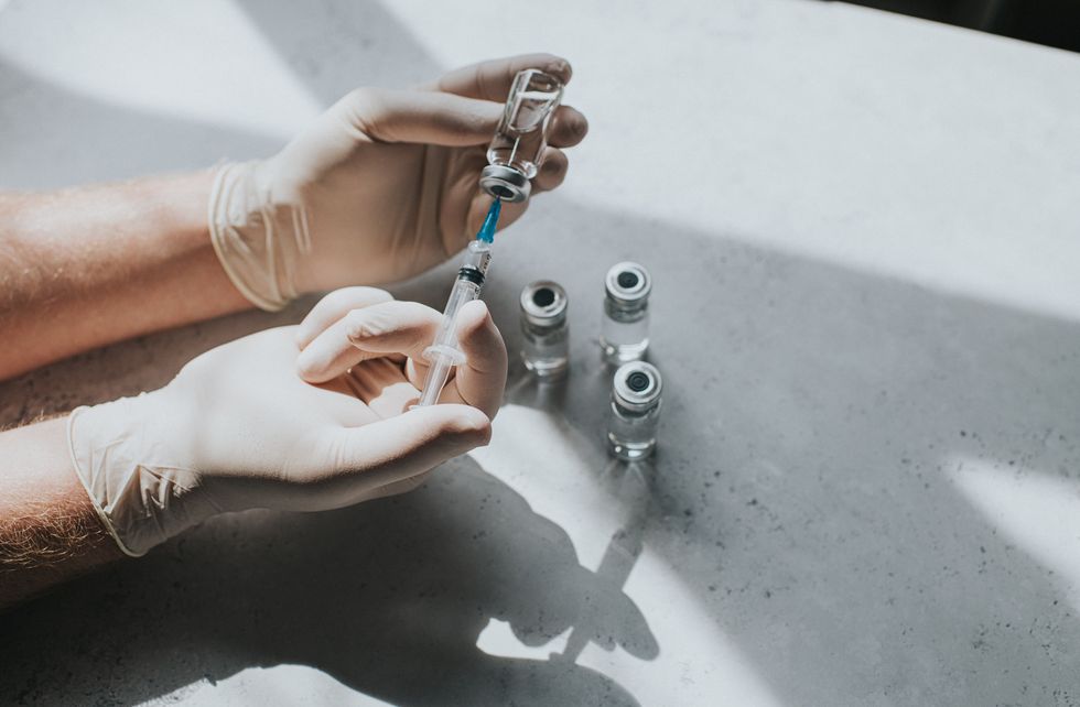 a hand wearing latex gloves hold a phial of clear liquid and a syringe the medical professional uses the syringe to extract the medicine from the glass bottle conceptual with space for copy