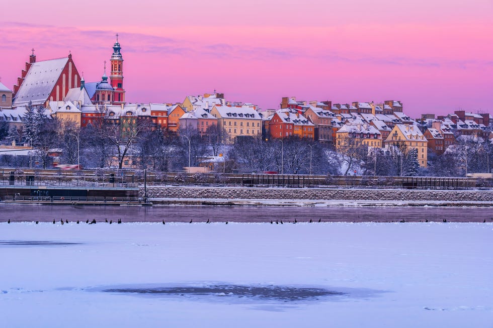 Poland, Masovian Voivodeship, Warsaw, Snow-covered bank of Vistula river at dawn with old town buildings in background a city with snow