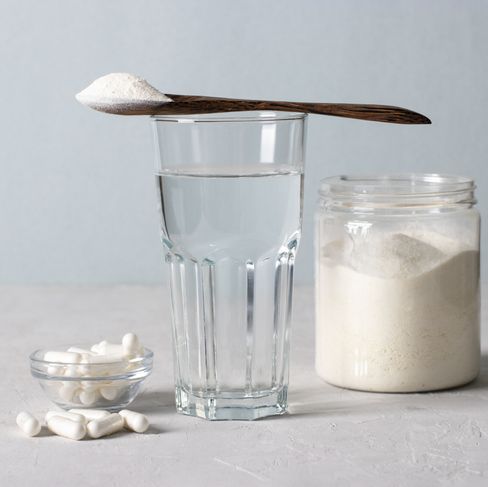 collagen powder in spoon on glass of water, collagen capsules and jar of powder on light blue background