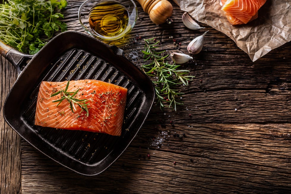 raw salmon steak in grill pan, salt, pepper, rosemary, olive oil and garlic on rustic oak table. top of view.