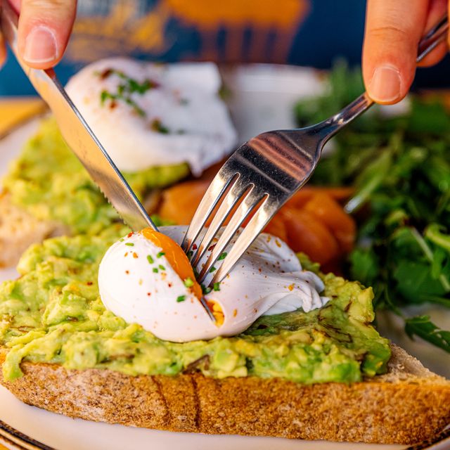 man eating avocado toast with poached egg and salmon, closeup view