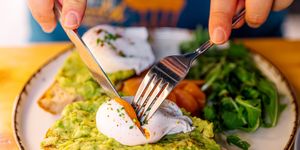 man eating avocado toast with poached egg and salmon, closeup view