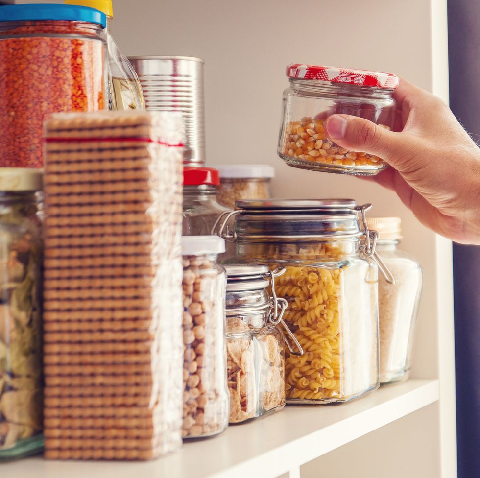 a man takes or places glass jars filled with legumes from a shelf in the pantry