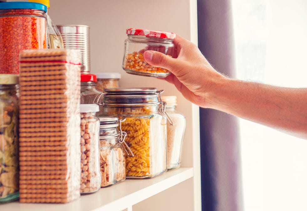 a man takes or places glass jars filled with legumes from a shelf in the pantry