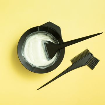 set for home or salon hair dyeing in the hands of a woman with gloves brushes and bowl for hair dye on yellow background