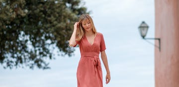 elegant blonde woman in coral colored summer dress walking about an old dalmatian town on stone paved pedestrian street, taking some time alone in the afternoon