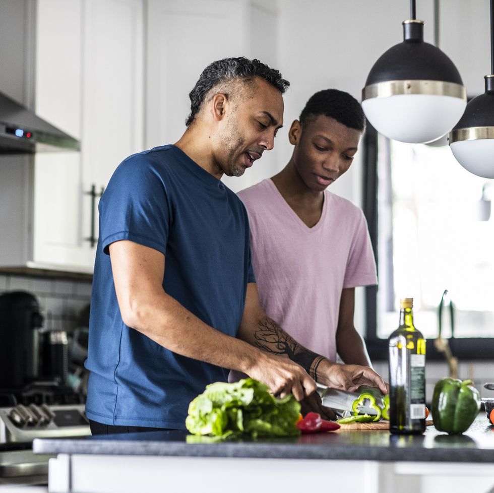 father and teenage son cooking together in kitchen