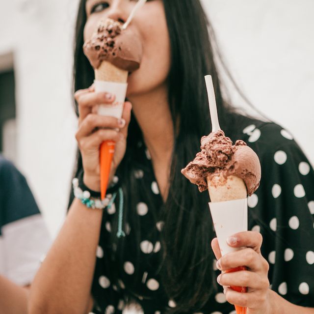 pretty latina stands on street holding melting chocolate cone ice cream while looking at camera
