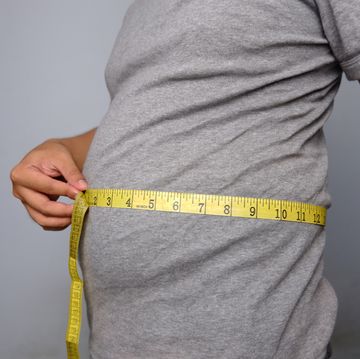 asian man wearing grey shirt measuring his waist with yellow waist measuring tape
