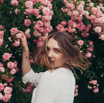 happy young woman spending summer day in garden of pink roses