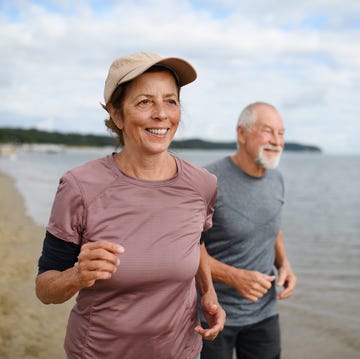 Active senior couple runners jogging outdoors on sandy beach by sea in early morning. active senior woman and man running outdoors sea