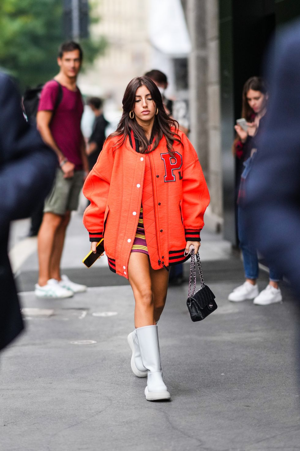 milan, italy   september 25 a guest wears gold earrings, a burgundy with yellow stripes short dress, a neon orange sport oversized bomber coat from philosophy, a black shiny quilted leather handbag from chanel, white leather ankle boots, outside the philosophy fashion show during the milan fashion week   spring  summer 2022 on september 25, 2021 in milan, italy photo by edward berthelotgetty images