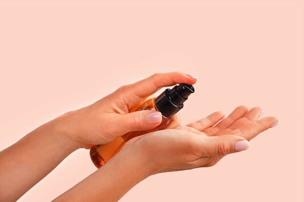 beautiful female hands holds bottle with natural organic face serum or essential organic oil on trendy peach pink color background caucasian woman hands body, hair skin care nature concept front view copy space close up