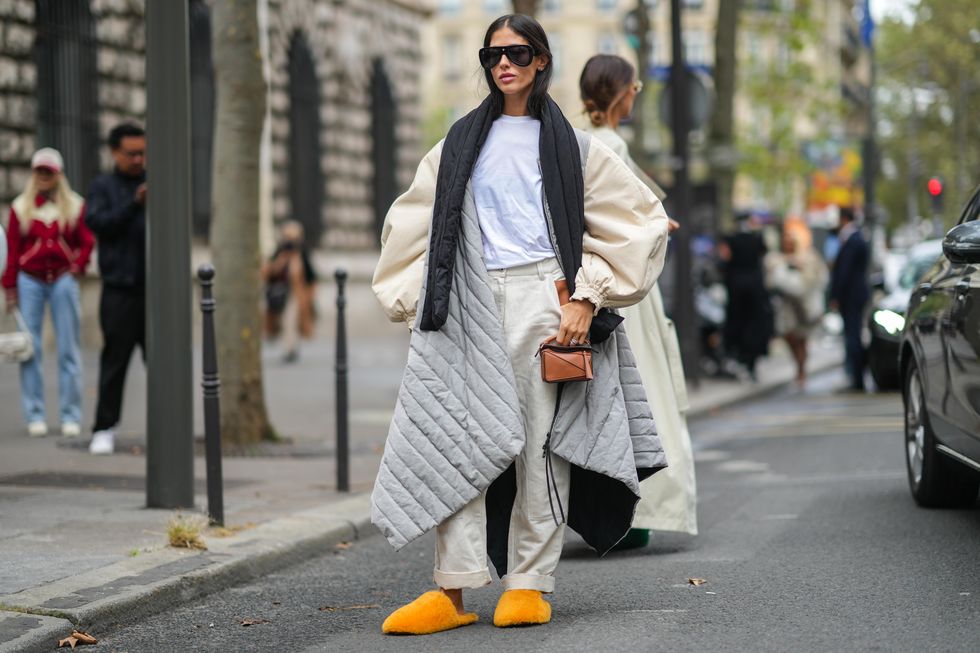 paris, france   october 01 gilda ambrosio wears black sunglasses, a white t shirt, a black puffy scarf, a half beige oversized puffy sleeves and half pale gray quilted oversized puffer jacket, beige high waist large pants, silver rings, a brown shiny leather small handbag form loewe, orange fluffy oversized mules  sandals, outside loewe, during paris fashion week   womenswear spring summer 2022, on october 01, 2021 in paris, france photo by edward berthelotgetty images