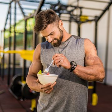 smiling young male athlete eating a vegetable salad at the gym