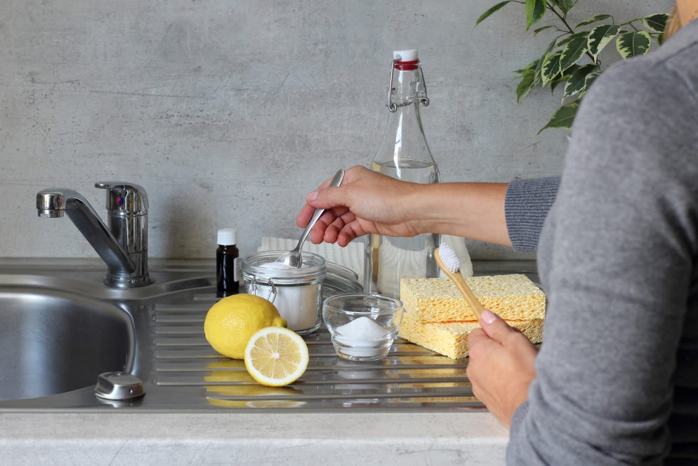 vinegar, bicarbonate of soda, lemon, sponge, bamboo toothbrush, cotton towels on the kitchen stainless stil sink next to the tap