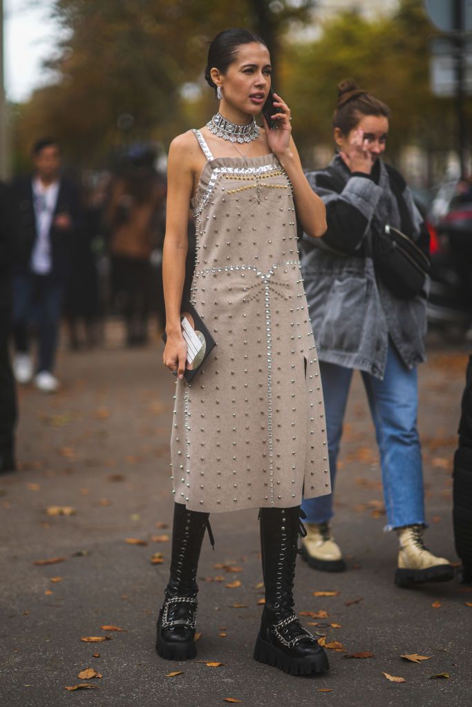 paris, france   october 05 a guest wears large necklace, a beige suede gold and silver nailed  studded ruffled borders slit  split midi dress, silver rings, black shiny leather lace knees boots with platform sole and silver chains from miu miu, outside miu miu, during paris fashion week   womenswear spring summer 2022, on october 05, 2021 in paris, france photo by edward berthelotgetty images