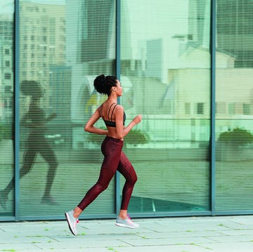 Young sportswoman runs past building with glass facade on street young sportswoman in stylish tracksuit runs past modern building with glass facade reflecting large city street side view