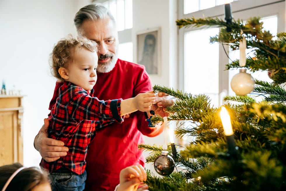 Ideas de fotografías familiares navideñas - El abuelo se une a su nieto mientras decora el árbol de Navidad.