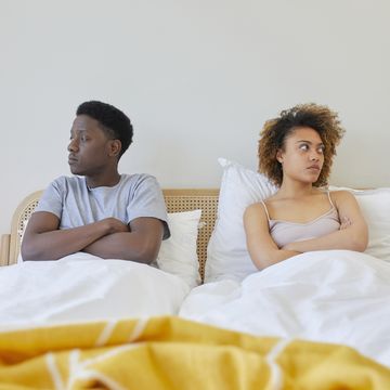 young couple on bed, they are looking away from each other and look irritated