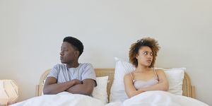 young couple on bed, they are looking away from each other and look irritated