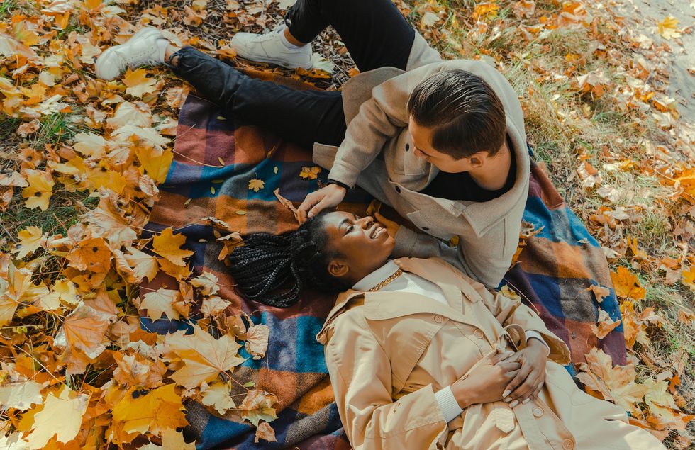 heterosexual mix raced couple laying on blanket in park in autumn