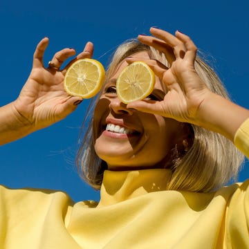 cheerful woman holding slice of lemon in front of eyes during sunny day cheerful woman holding slice of lemon in front of eyes during sunny day