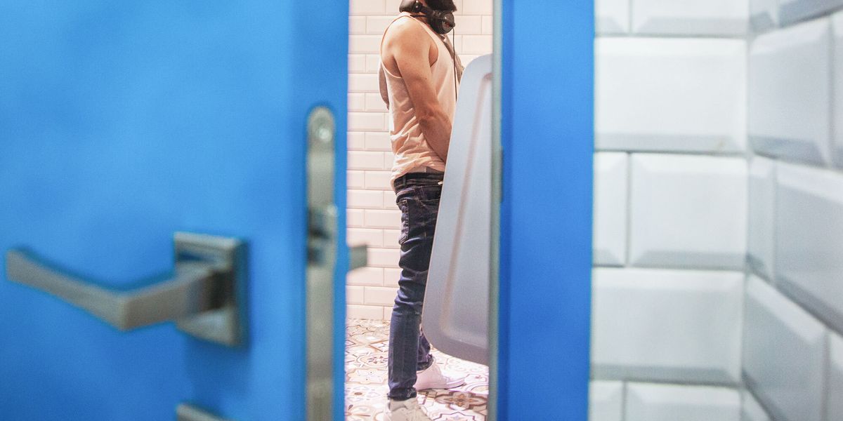 man at urinal as seen through slightly open door