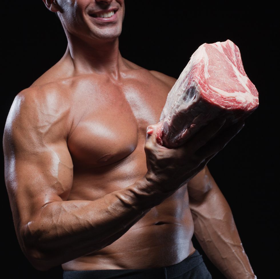 muscular caucasian man holding raw beef, smiling, studio shot