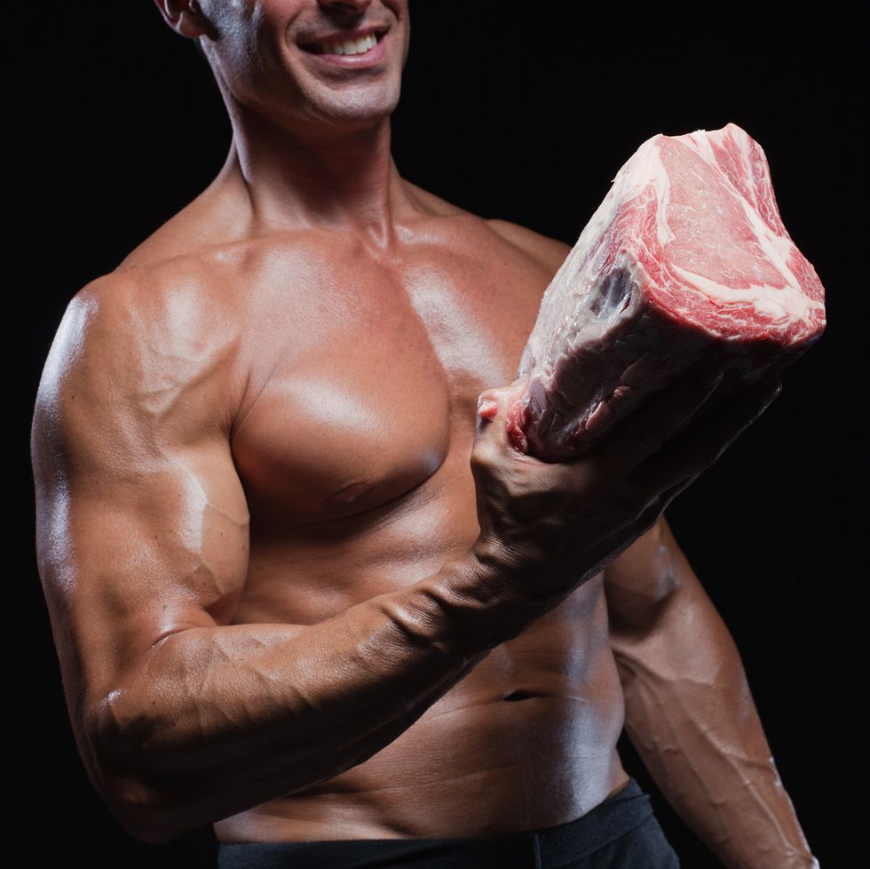 muscular caucasian man holding raw beef, smiling, studio shot