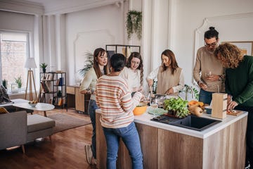 group of people, diverse male and female friends preparing a meal and drinking wine together in domestic kitchen,