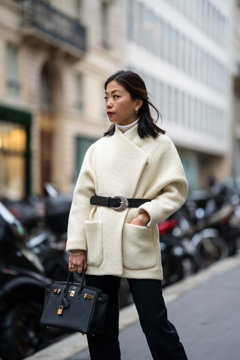 paris, france november 30 may berthelot wears gold earrings from leo sedim, a white ribbed wool turtleneck pullover, a white latte coat with a black leather belt from bash, black denim flared pants, black grained leather birkin handbag form hermes, gold rings, during a street style fashion photo session, on november 30, 2021 in paris, france photo by edward berthelotgetty images