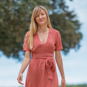 beautiful blonde woman in coral colored summer dress wandering around an old dalmatian town on stone paved pedestrian zone and smiling at camera, relaxation on solo vacation